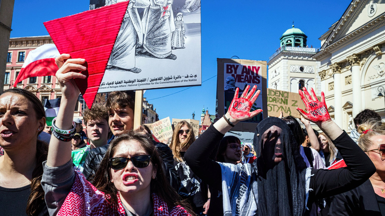 A group of pro-Palestinian protesters gather holding flags, signs, and large red triangles. 