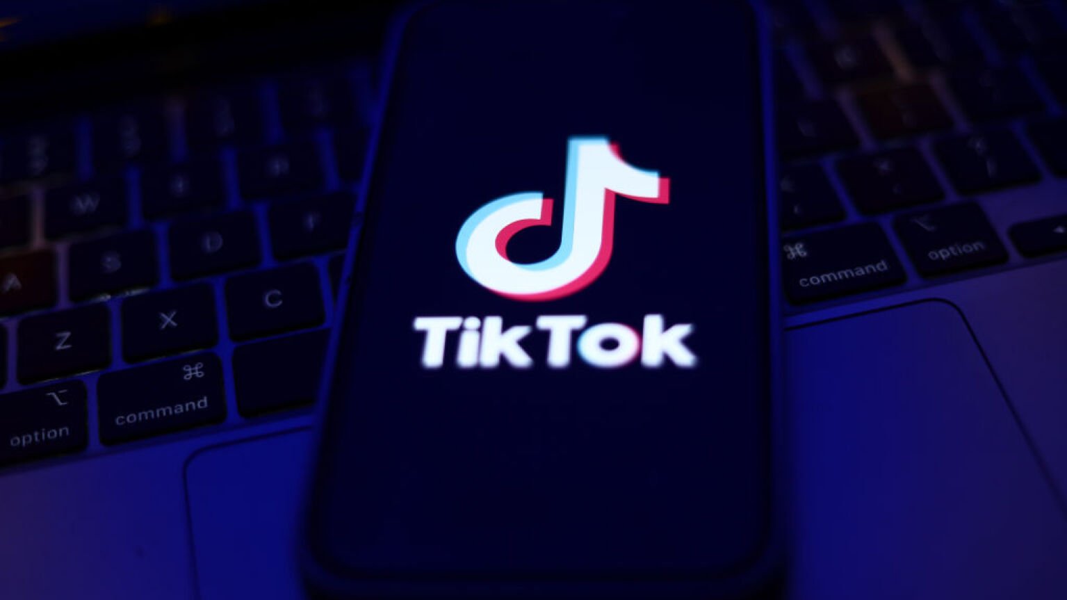 TikTok logo displayed on a phone screen and a laptop keyboard 