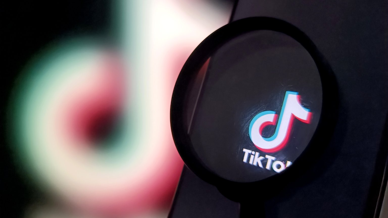 A magnifying glass magnifies a TikTok logo on a phone screen.