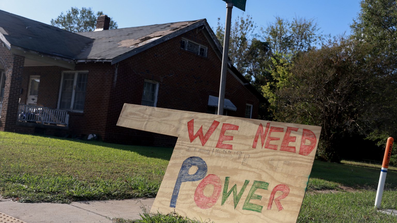 A wooden sign that reads "We need power" on the lawn outside of a home.