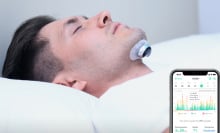 Person in white bed with device attached to chin and picture of phone showing data in front of them