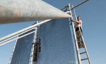 Two men stand on ladders to tend a fog collecting device that resembles a net.