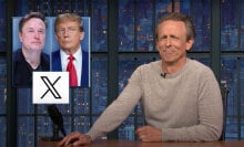 A man sits behind a talk show desk. In the top-left is an image of two other men.