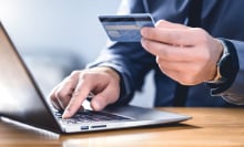 A man on a computer is using his credit card to purchase something.