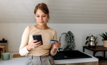 Person standing against counter in kitchen looking at gift card and smart phone