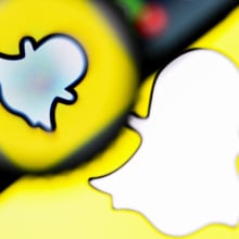 A snapchat logo with a magnifying glass and a phone hovering over it. 