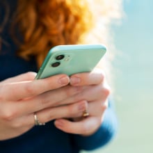 Close up of red-haired woman using smart phone with turquoise cover. 