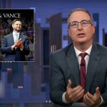 A man in a suit sits behind a talk show desk. In the top-left corner is an image of two other men.