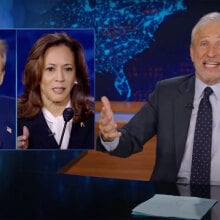 A man in a suit sits behind a talk show desk. In the top-left is an image of a man and woman.