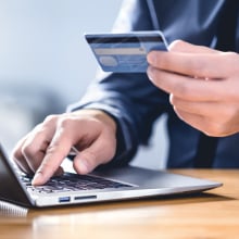 A man on a computer is using his credit card to purchase something.