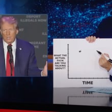 A man sits behind a talk show desk holding a chart. In the top-left is an image of another man wearing a suit.