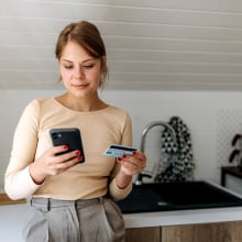 Person standing against counter in kitchen looking at gift card and smart phone