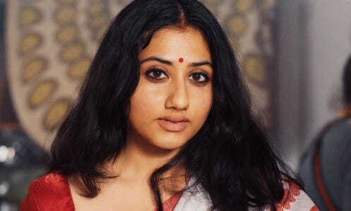 A woman wearing a sari and a red bindi looks into the camera.