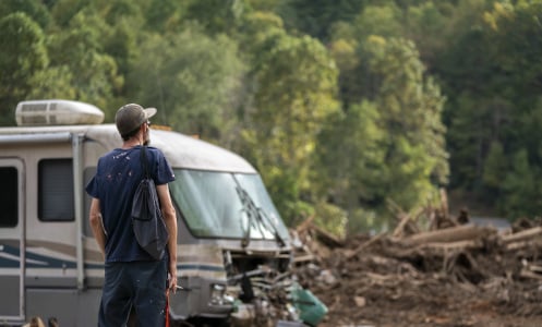 A man stares out at a piece of land full of debris, including the rubble of a home and a destroyed RV.