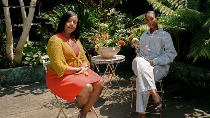 A still of two women speaking in a garden.