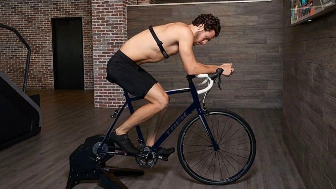 shirtless man wearing chest heart rate monitor on exercise bike