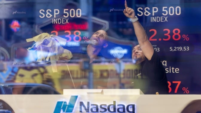 Two men at the NASDAQ stock exchange point at falling numbers on a screen. 