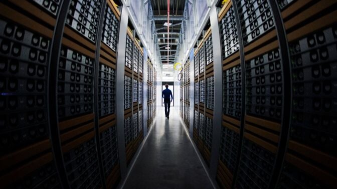 A man in silhouette, walking through racks of computers in a data center.