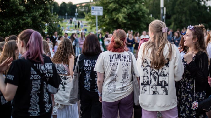 Taylor Swift fans decked out in merch standing in a crowd. 