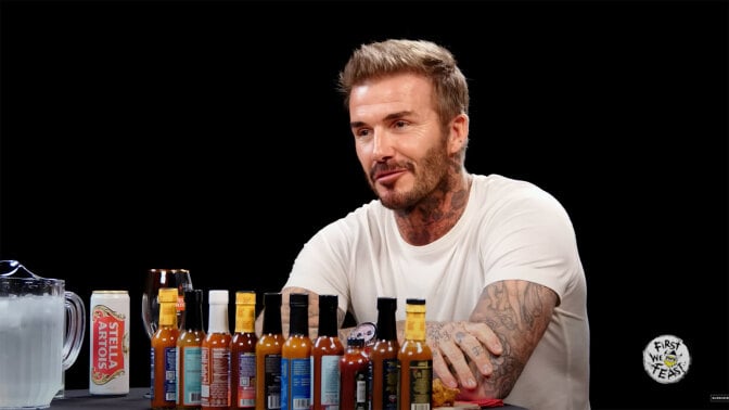 A man sits at a table covered with hot sauce in a dark room.