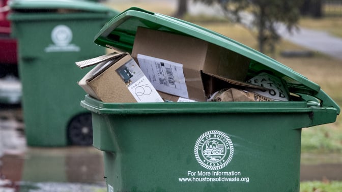 A green recycling bin with the city of Houston logo, full of cardboard boxes. 