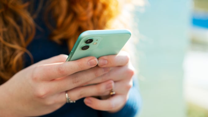 Close up of red-haired woman using smart phone with turquoise cover. 