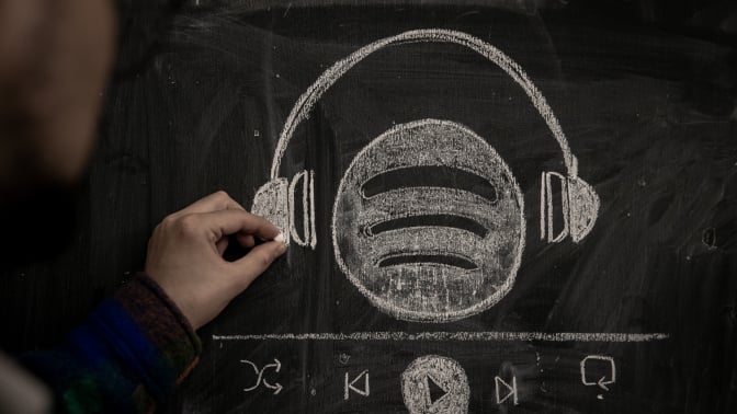 A person drawsingthe Spotify logo wearing a pair headphones in chalk. 