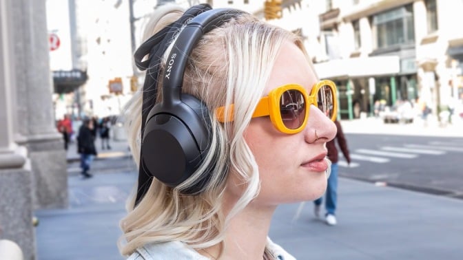 young woman in yellow sunglasses wearing Sony headphones on city street