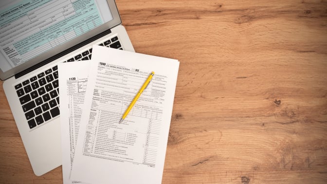 Tax paperwork on a table next to a laptop.