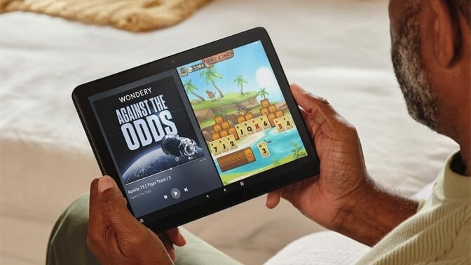 a person holds an Amazon fire HD 10 tablet while sitting on a cream colored couch