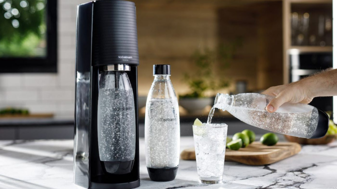 Person pouring sparkling water into glass next to SodaStream sparkling water maker on countertop