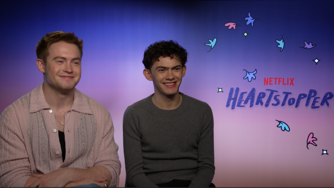 Left to right: Kit Connor and Joe Locke sit next to each other against a colourful 'Netflix Heartstopper' background